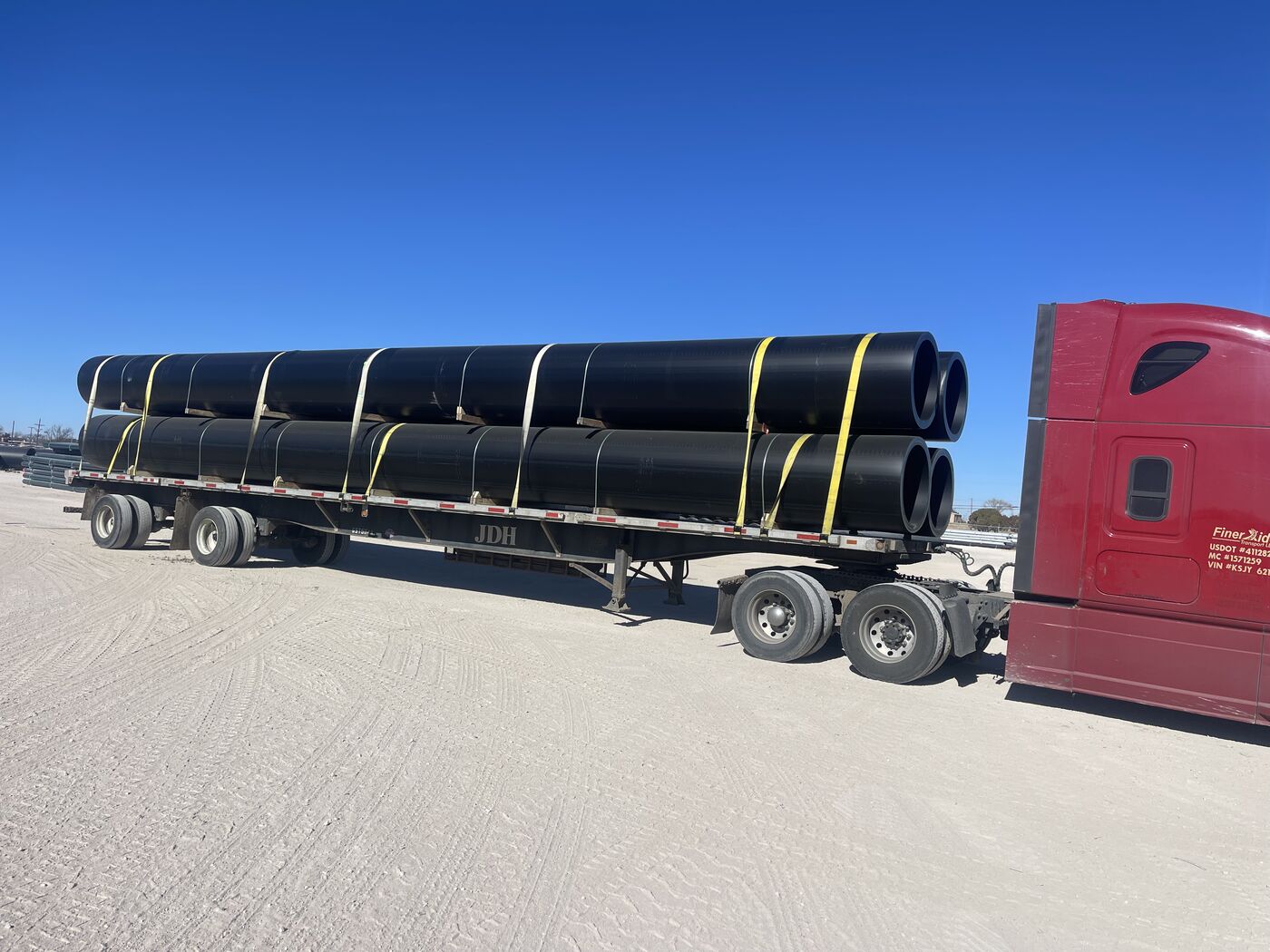 Close-up of bundled black pipe strapped to flatbed trailer in oilfield yard