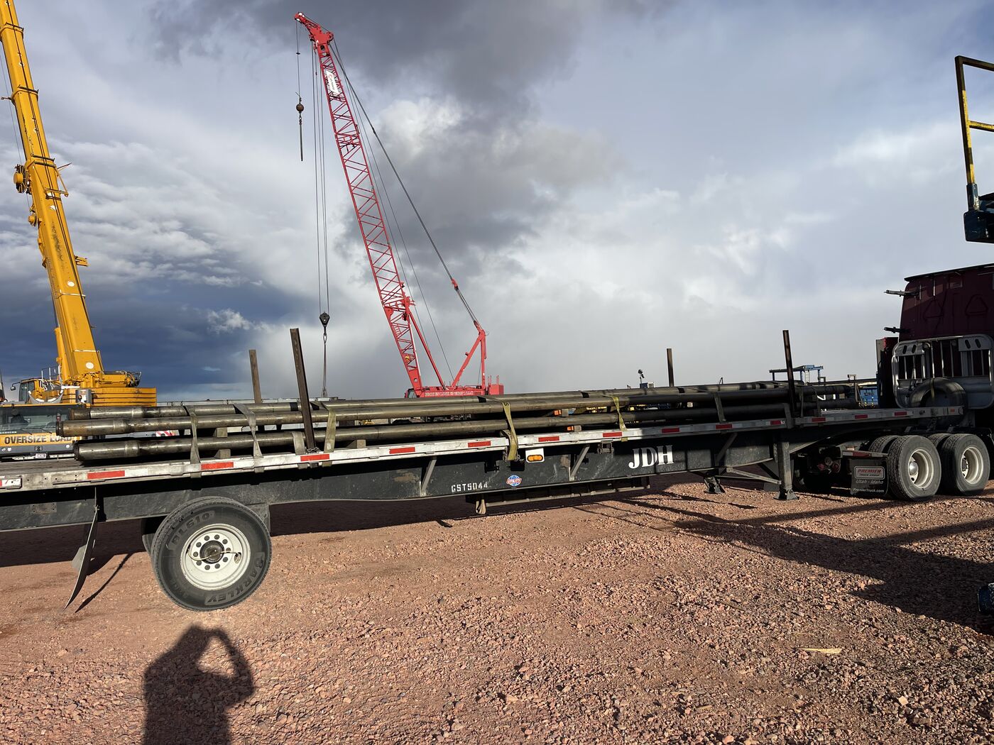 Flatbed being loaded by red crane at oilfield site with dramatic storm clouds overhead