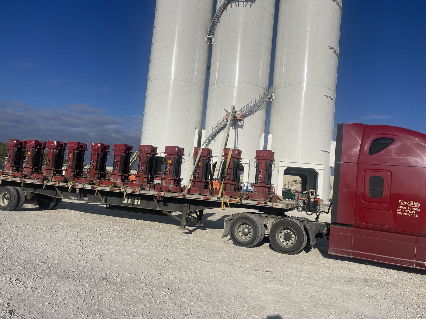 Flatbed loaded with oilfield wellhead equipment staged in front of frac sand silos in the Permian Basin