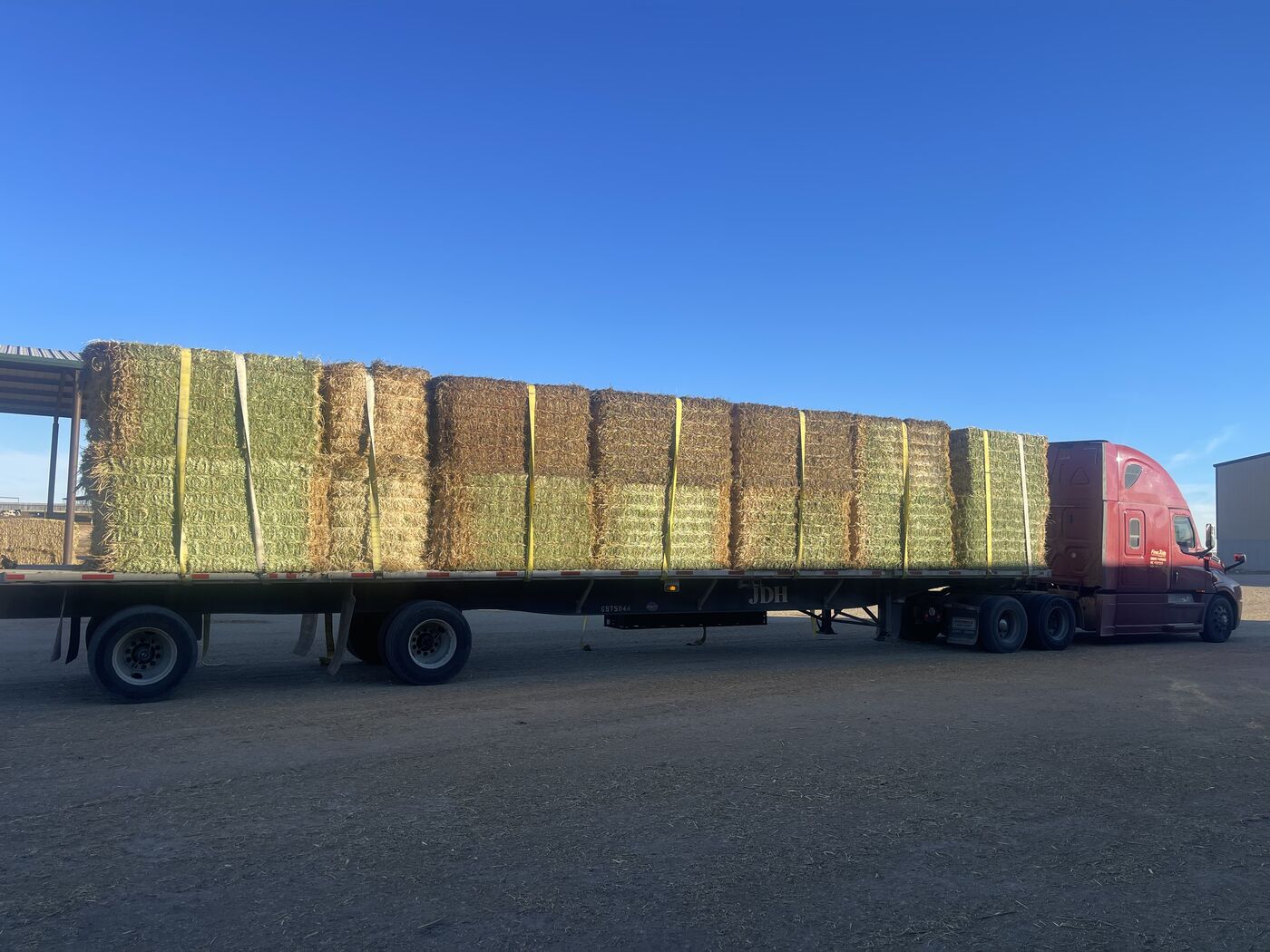 Red Freightliner Cascadia flatbed fully loaded with hay bales in West Texas