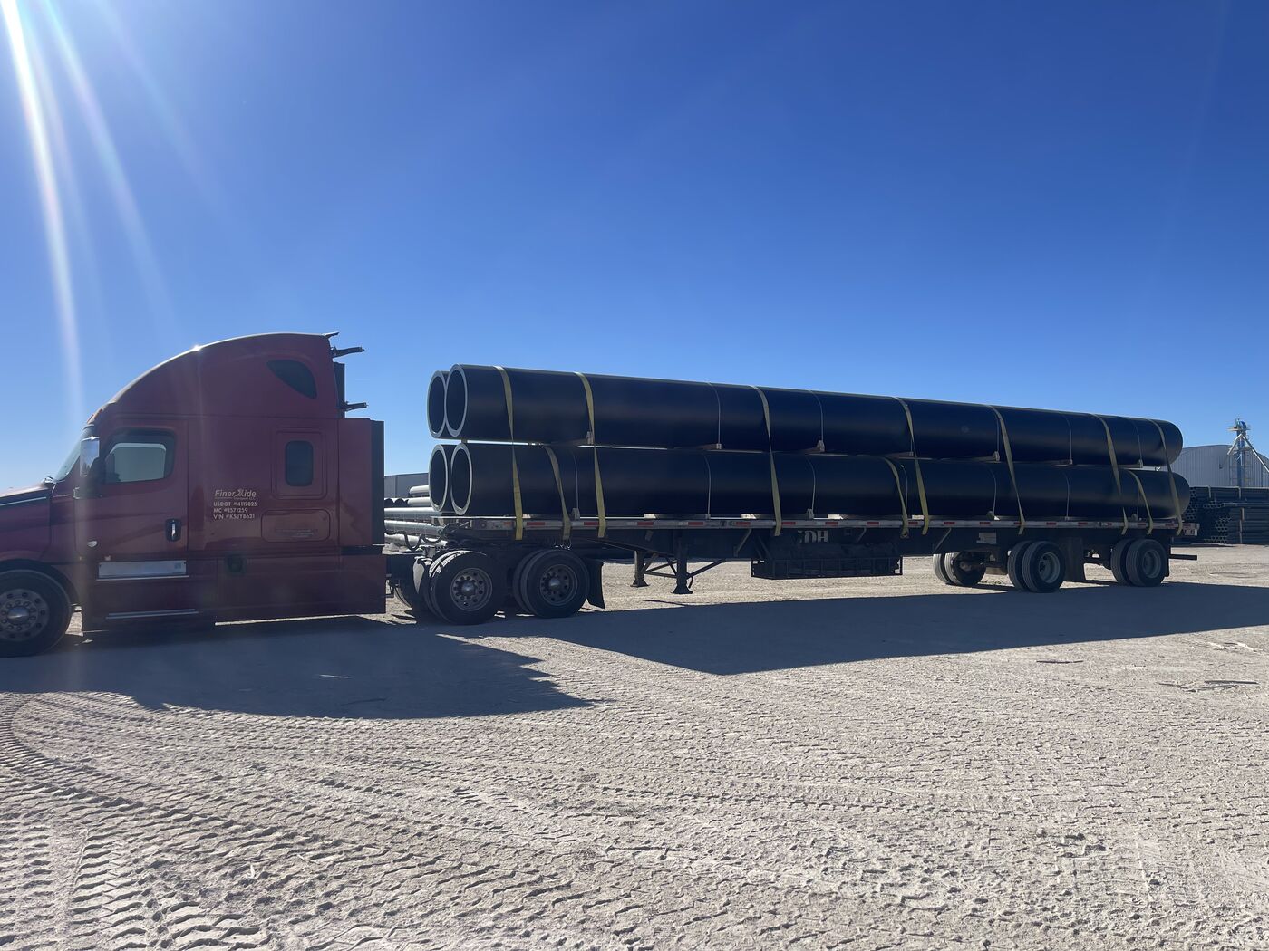 Large diameter black pipe bundled and strapped on flatbed trailer with Freightliner Cascadia