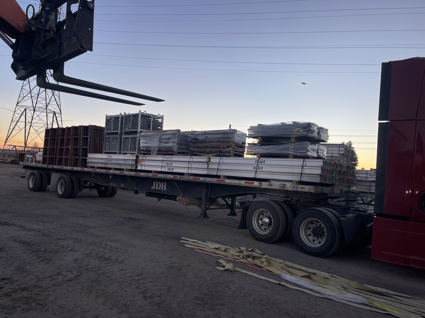 Flatbed loaded with bundled structural steel I-beams being loaded at dusk