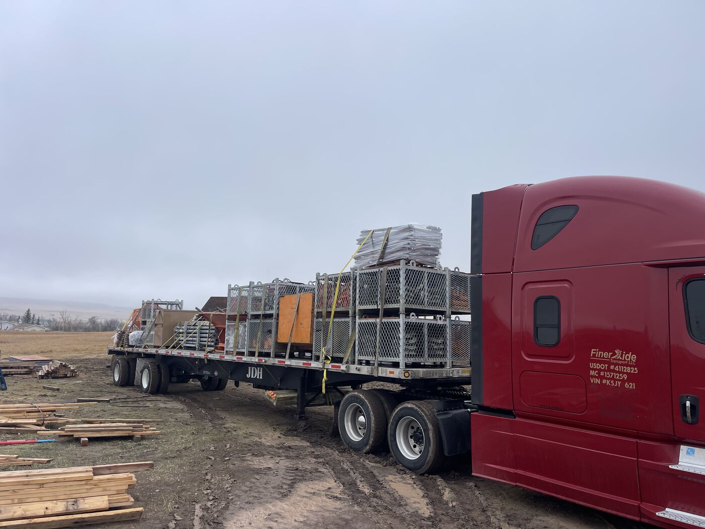 Red Freightliner Cascadia 126 with USDOT and MC numbers visible on the cab hauling construction equipment