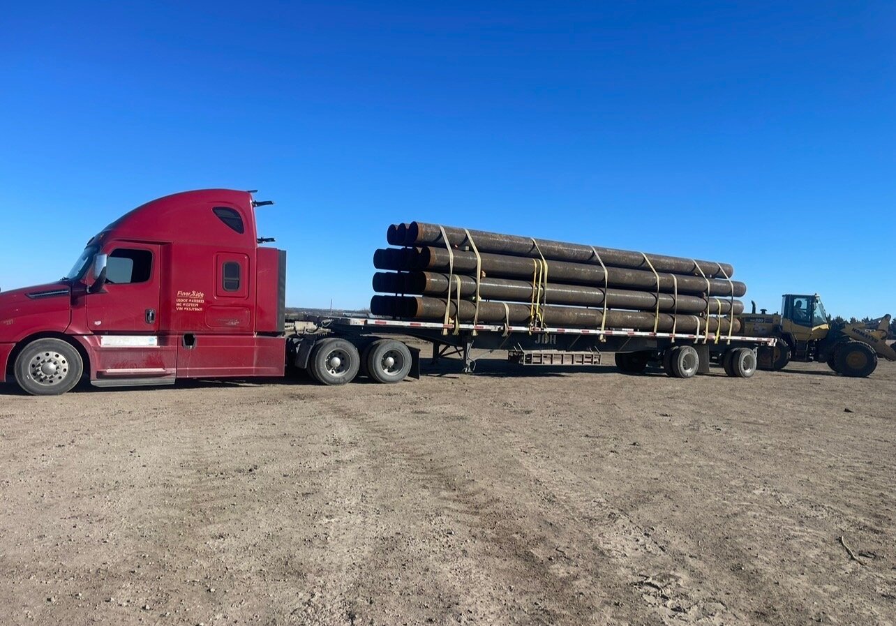 FinerXide Transport red Freightliner Cascadia 126 with 53-foot flatbed loaded with large diameter pipe in the Permian Basin — USDOT #4112825, MC #1571259